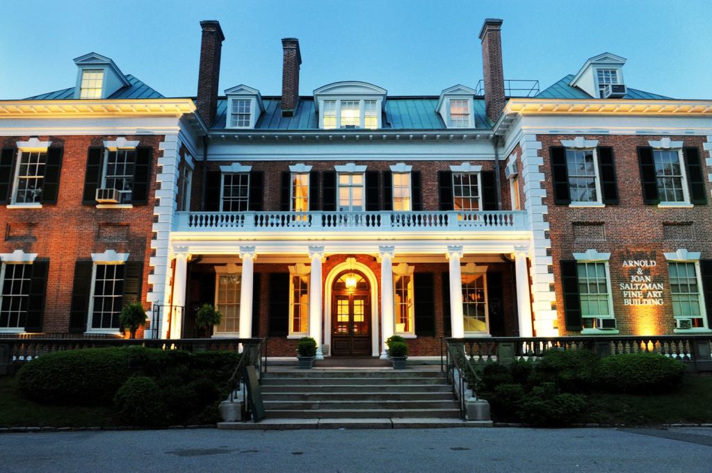 기둥과 여러 개의 굴뚝이 있는 웅장한 벽돌 저택으로, 해질녘에 볼 수 있습니다. 계단은 정문으로 이어집니다.