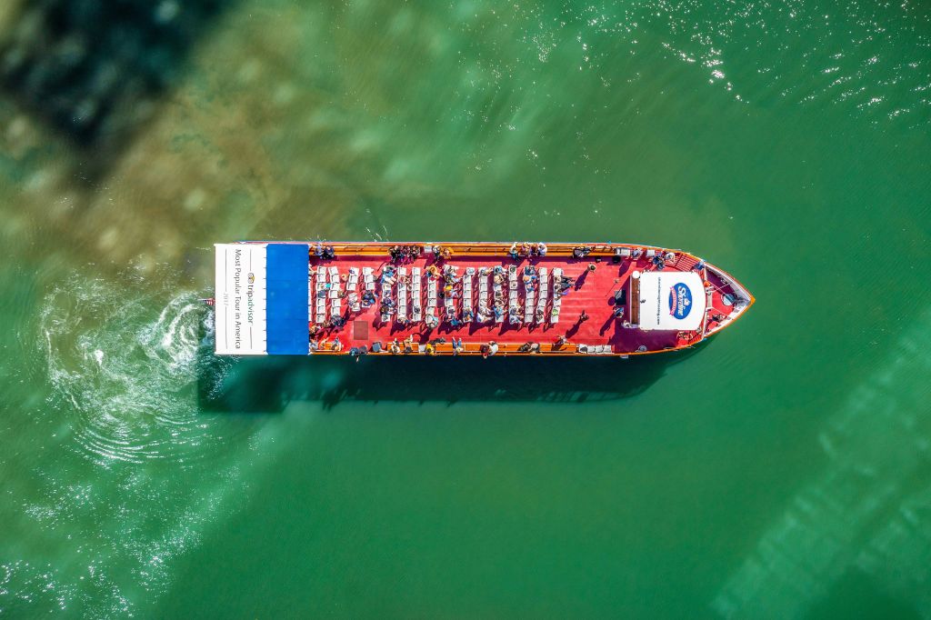 좌석이 있고 사람들로 가득 찬 녹색 물 위를 이동하는 붉은 여객선의 공중 전망.