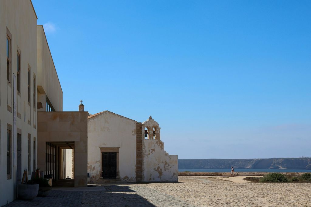 밝은 날 종탑이 있는 작은 흰색 예배당으로, 자갈이 깔린 지역 근처에 있으며 먼 바다가 내려다보입니다.