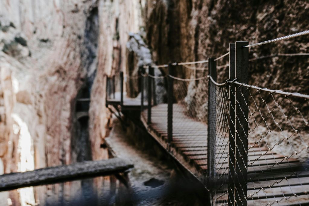 난간이 있는 좁은 나무 통로가 바위 절벽을 따라 이어지며 아래로 가파른 물방울이 보입니다.
