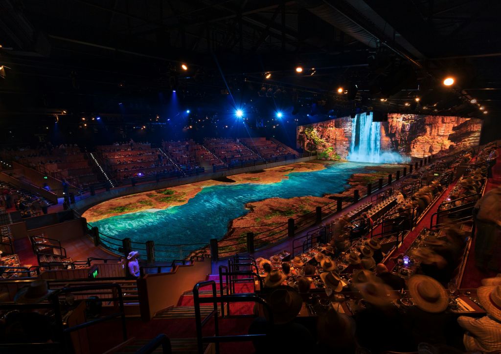 층층이 쌓인 좌석과 폭포와 강 풍경이 생생하게 투영된 무대가 있는 대형 실내 극장.