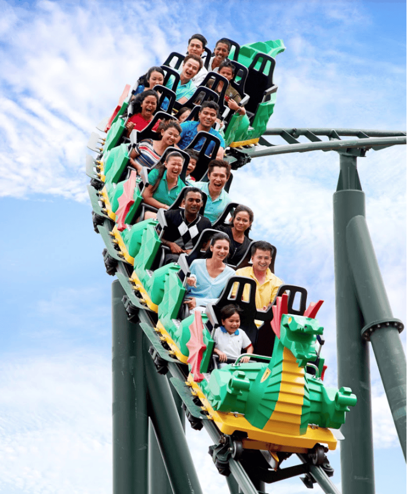 용을 주제로 한 롤러코스터를 타고 밝고 부분적으로 흐린 하늘 아래에서 미소를 짓고 흥분을 표현하는 사람들.