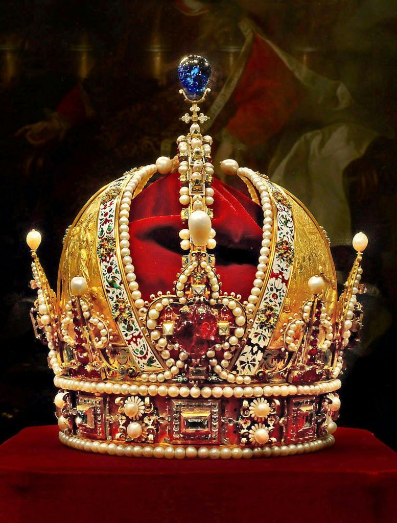 진주, 보석, 레드 벨벳 쿠션에 세팅된 디테일한 패턴으로 장식된 정교하게 디자인된 골드 크라운.