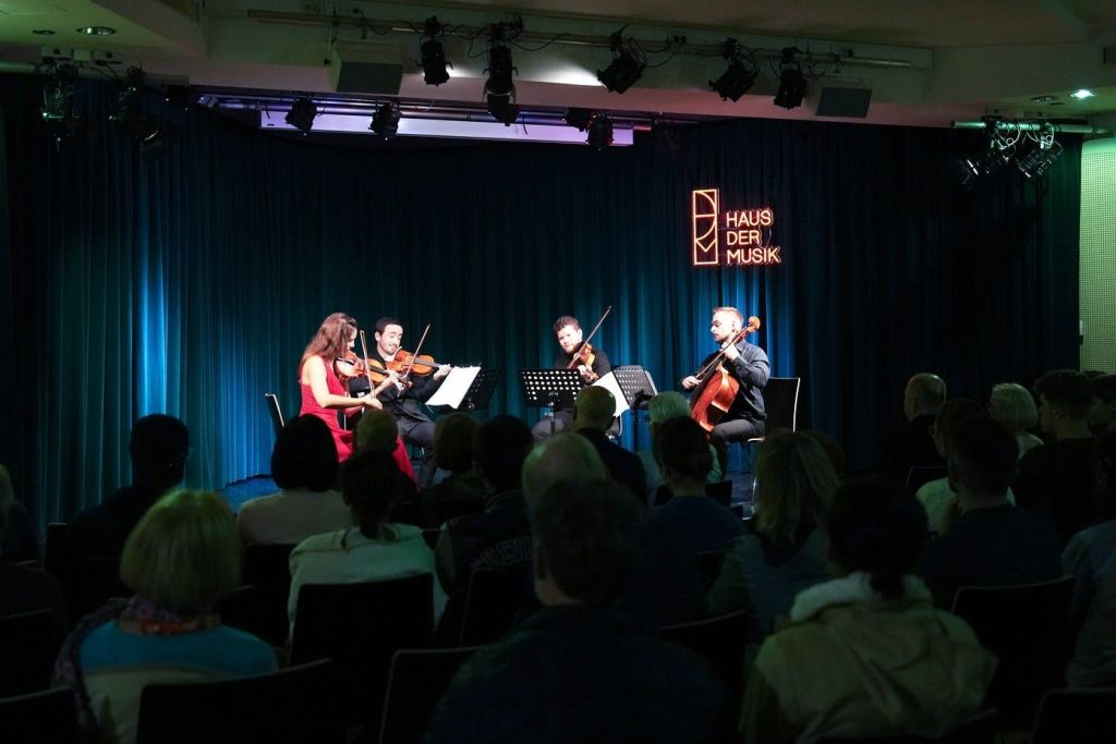현악 사중주단이 무대에서 관객을 앞에 앉힌 채 공연합니다. "Haus der Musik" 이라는 표지판이 있습니다.