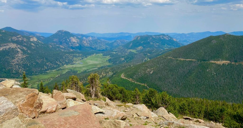 바위가 많은 전경, 푸른 숲이 우거진 비탈, 저 멀리 펼쳐진 계곡이 있는 경치 좋은 산 풍경.