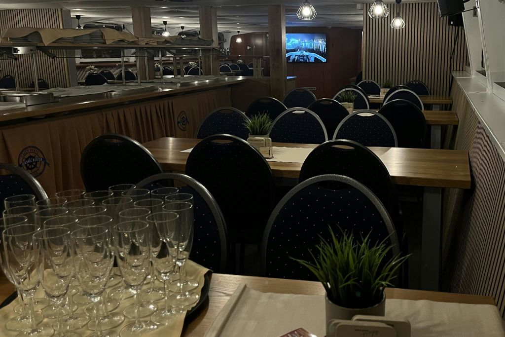 식탁에는 유리잔과 화분, 어두운 색상의 의자가 놓여 있고, 배경에는 화면이 보입니다.