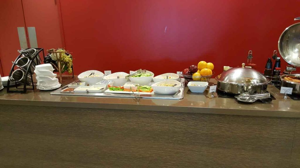 빨간 벽을 배경으로 카운터에 샐러드, 과일, 애피타이저가 담긴 다양한 그릇이 놓인 뷔페.
