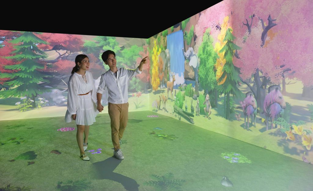 실감나는 자연을 주제로 한 디지털 프로젝션이 있는 방을 거닐며 손을 잡고 미소를 짓는 커플.