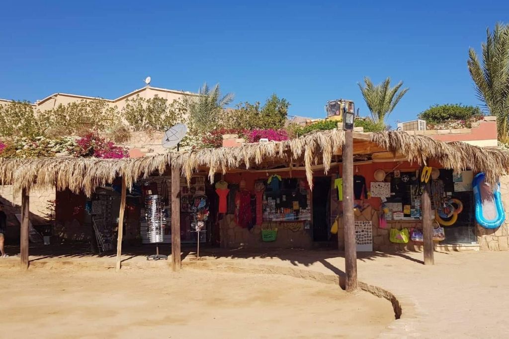 나무와 푸른 하늘을 배경으로 의류, 기념품 및 기타 물품을 판매하는 초가 지붕이 있는 야외 시장 노점.