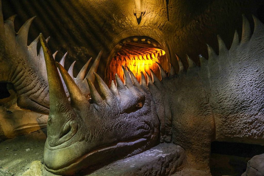 어두운 동굴 같은 분위기의 따뜻한 조명 아래에서 눈에 띄는 스파이크를 가진 생물의 커다란 석조 조각.