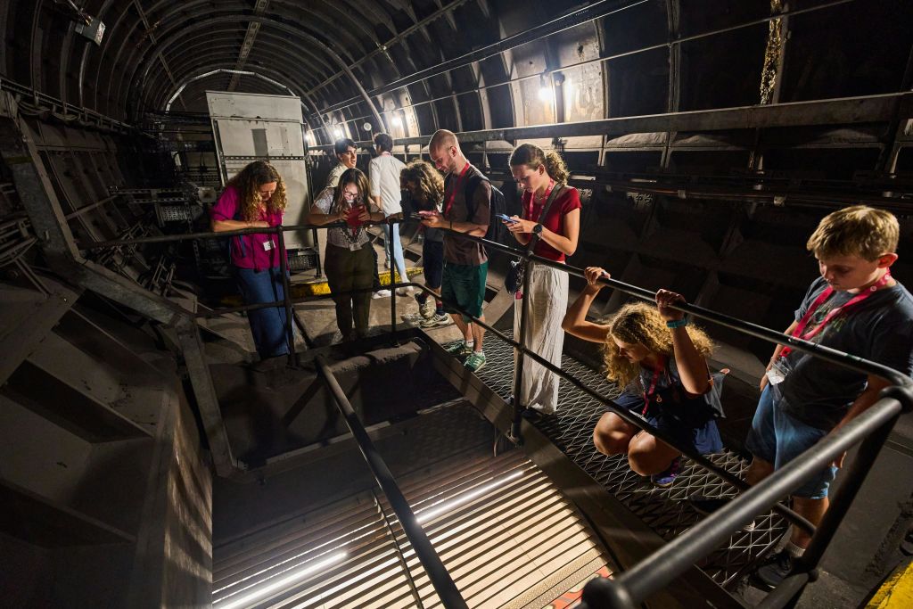 지하 터널을 탐험하고, 금속 통로에 서서, 아래를 내려다보고, 사진을 찍거나 관찰하는 사람들도 있습니다.