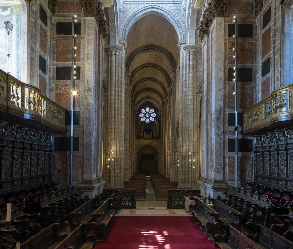 높은 아치, 화려한 기둥, 나무 퓨, 레드 카펫, 원형 스테인드글라스 창문이 있는 대형 대성당의 내부.