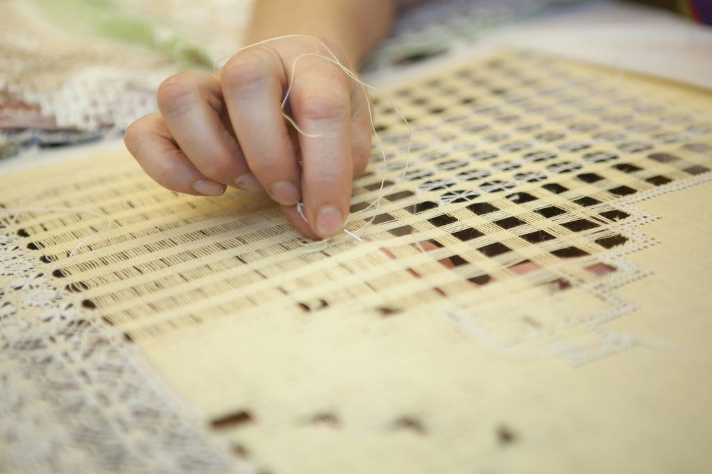 회백색의 격자 무늬 패브릭을 통해 얇은 실을 손으로 짜는 클로즈업.