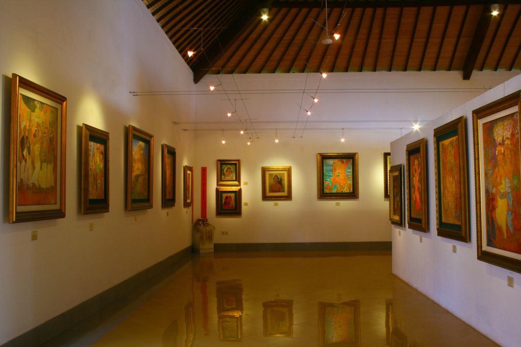 흰색 벽, 나무 천장, 타일 바닥, 천장 조명에 액자 그림이 있는 작은 아트 갤러리가 미술품을 비춥니다.