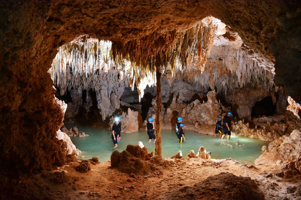 헬멧과 전조등을 착용한 사람들은 수많은 종유석과 종유석이 있는 동굴 안의 허리 깊이의 물을 헤치고 지나갑니다.