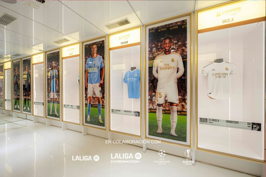 축구 선수의 실물 크기 포스터, 팀 유니폼, 축구 리그 및 토너먼트 로고가 있는 디스플레이 케이스.