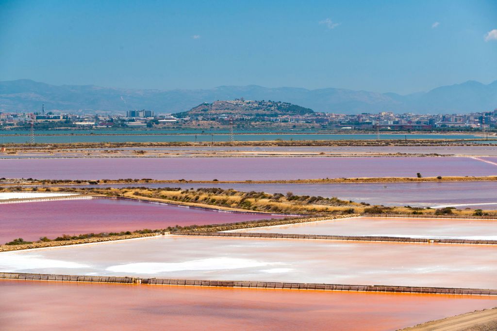 분홍색, 보라색, 흰색 색조의 다색 소금 증발 연못은 언덕을 배경으로 한 도심 근처에 있습니다.