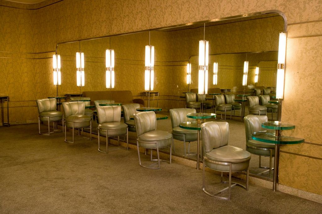 녹색 가죽 의자, 원형 유리 테이블, 커다란 거울에 반사되는 조명 벽 조명이 있는 복고풍 라운지.