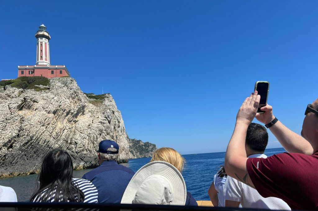 보트를 타고 있는 몇몇 사람들은 맑고 푸른 하늘 아래 꼭대기에 빨간색 건물이 있는 바위 절벽을 관찰합니다.