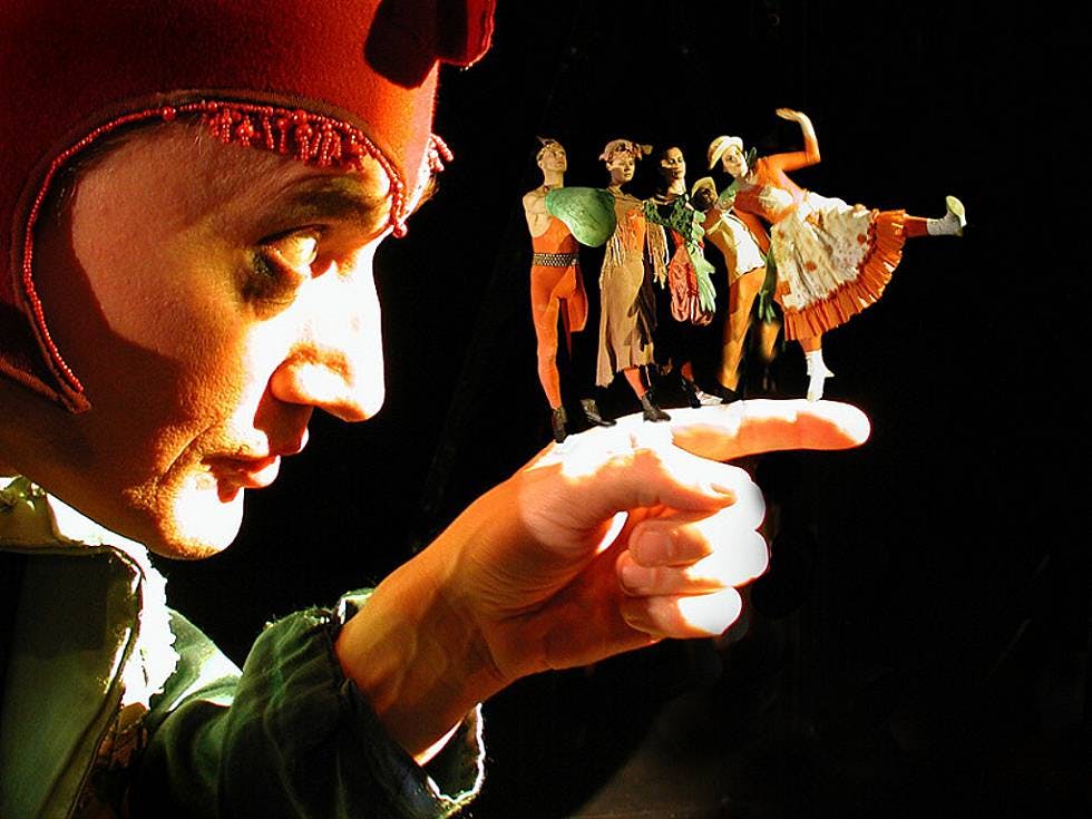 빨간 모자를 쓴 사람이 손가락을 보는데, 작고 밝은 옷을 입은 댄서들이 공연을 하는 것처럼 보입니다.