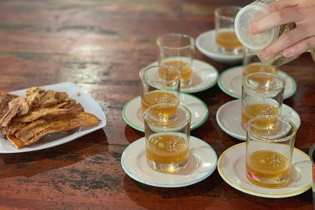 접시에 담긴 작은 맥주 몇 잔이 테이블에 채워지고 있으며, 옆에는 튀긴 스낵이 놓여 있습니다.