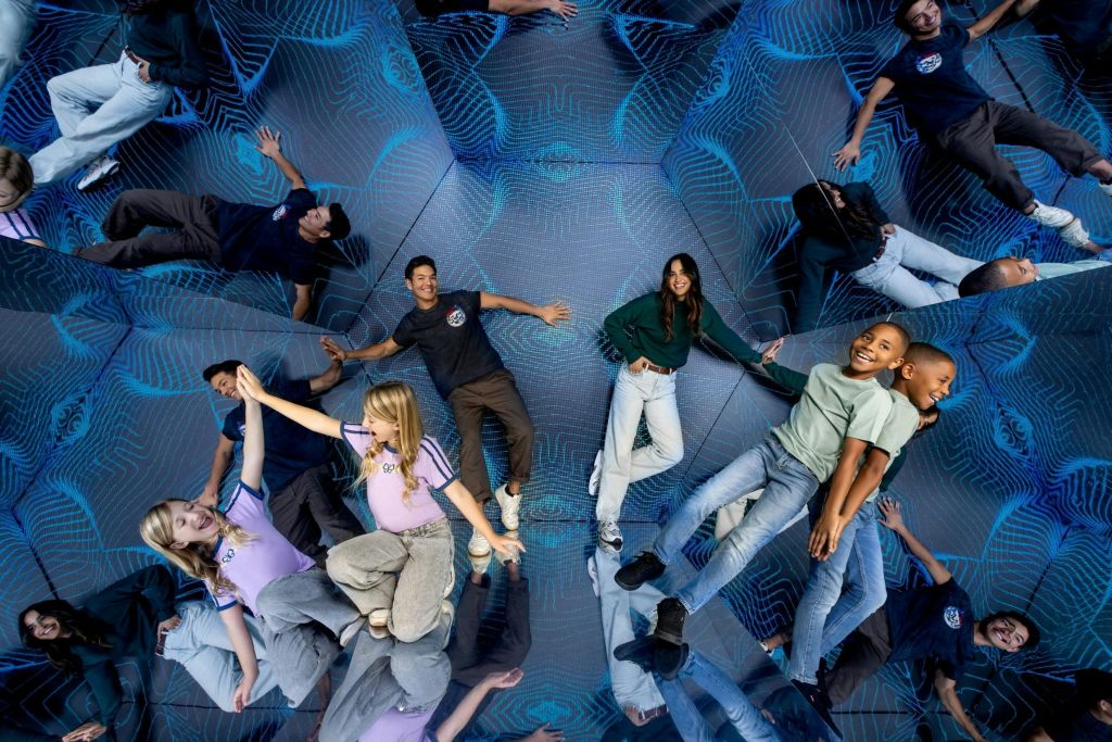 벽에 반사 표면과 기하학적 파란색 패턴이 있는 방에 서서 포즈를 취하는 사람들의 그룹.