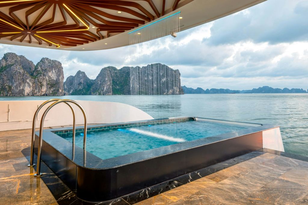 석회암 섬과 흐린 하늘이 있는 잔잔한 만이 내려다보이는 폭포가 있는 야외 직사각형 수영장.