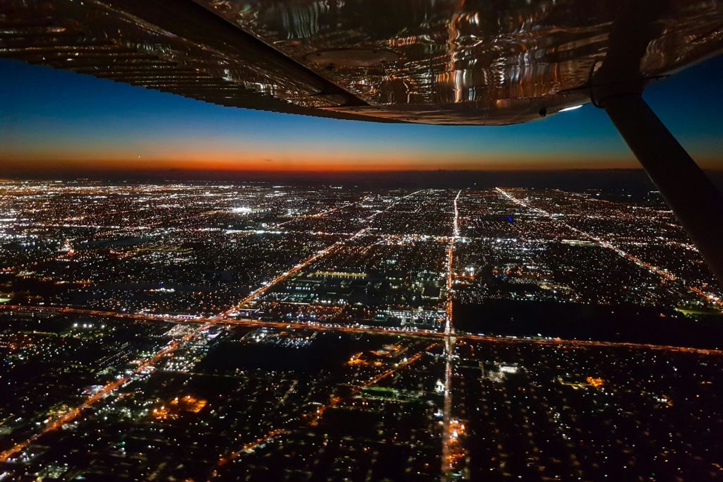 비행기 창문으로 조명이 켜진 거리와 건물이 있는 해질 무렵 도시의 공중 전망을 감상할 수 있습니다.