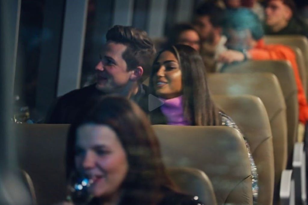 부드러운 조명으로 버스에 앉아 미소를 짓고 대화하는 사람들. 이미지 중간에 있는 남성과 여성에게 초점을 맞춥니다.