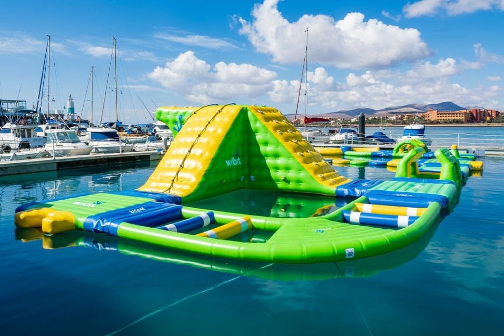 정박한 보트와 산을 배경으로 정박지에 떠있는 노란색과 녹색 미끄럼틀이 있는 팽창식 물 장애물 코스.