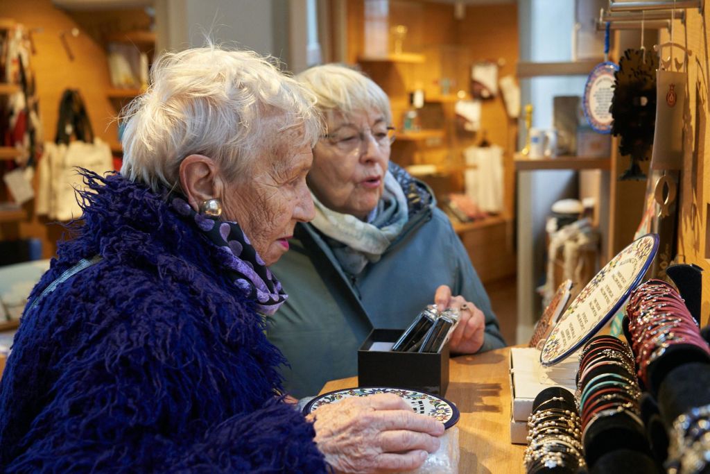 두 명의 노인 여성이 매장에서 물건을 자세히 보며 쇼핑하고 있습니다. 다양한 제품이 담긴 선반이 배경으로 보입니다.