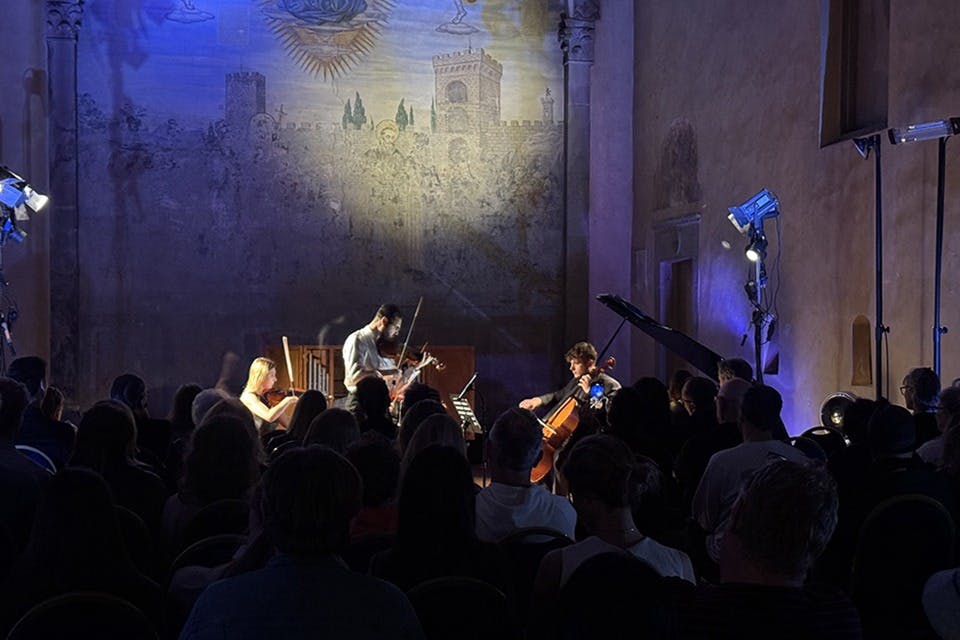 조그만 음악 앙상블이 벽에 페인트가 칠해져 있고 앞에 관객이 있는 조명이 희미한 방에서 무대에서 공연합니다.