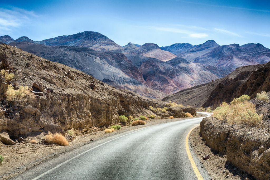 맑고 푸른 하늘 아래 산을 배경으로 바위투성이의 사막 풍경을 가로지르는 구불구불한 도로.