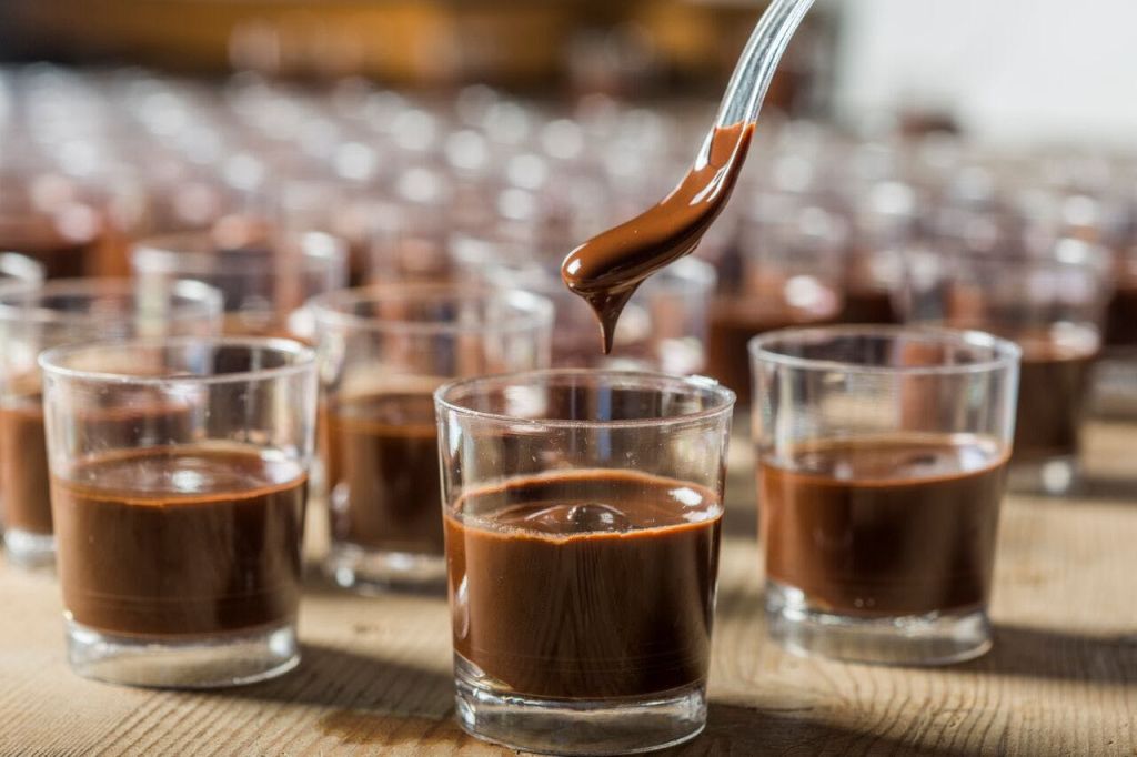 숟가락이 초콜릿으로 가득 찬 수많은 비슷한 잔으로 둘러싸인 작은 잔에 초콜릿을 떨어뜨립니다.