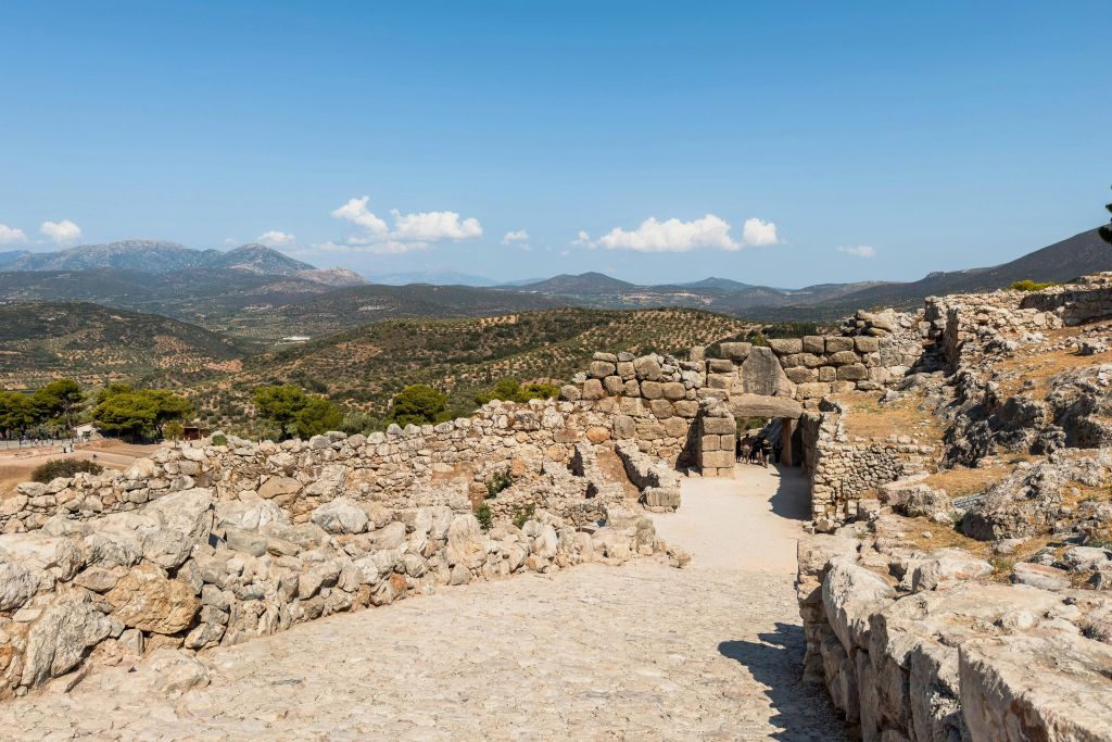 밝은 푸른 하늘 아래 언덕 풍경으로 둘러싸인 아치형 관문이 있는 고대 석조 유적지.