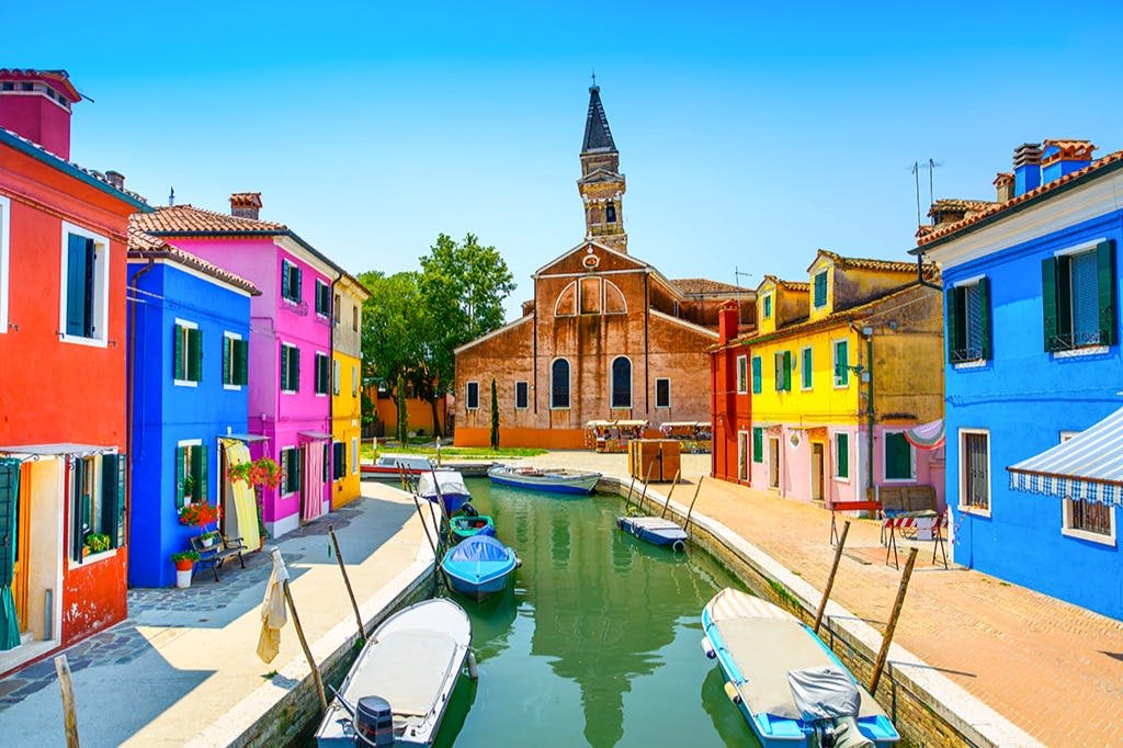 운하에는 형형색색의 집들이 줄지어 있고, 물 위에는 작은 보트가 있으며, 높은 첨탑을 배경으로 교회가 있습니다.