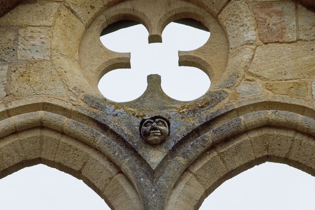중앙에 얼굴이 있고 그 위로 콰트르포일이 열려 있는 조각된 석조 아치.