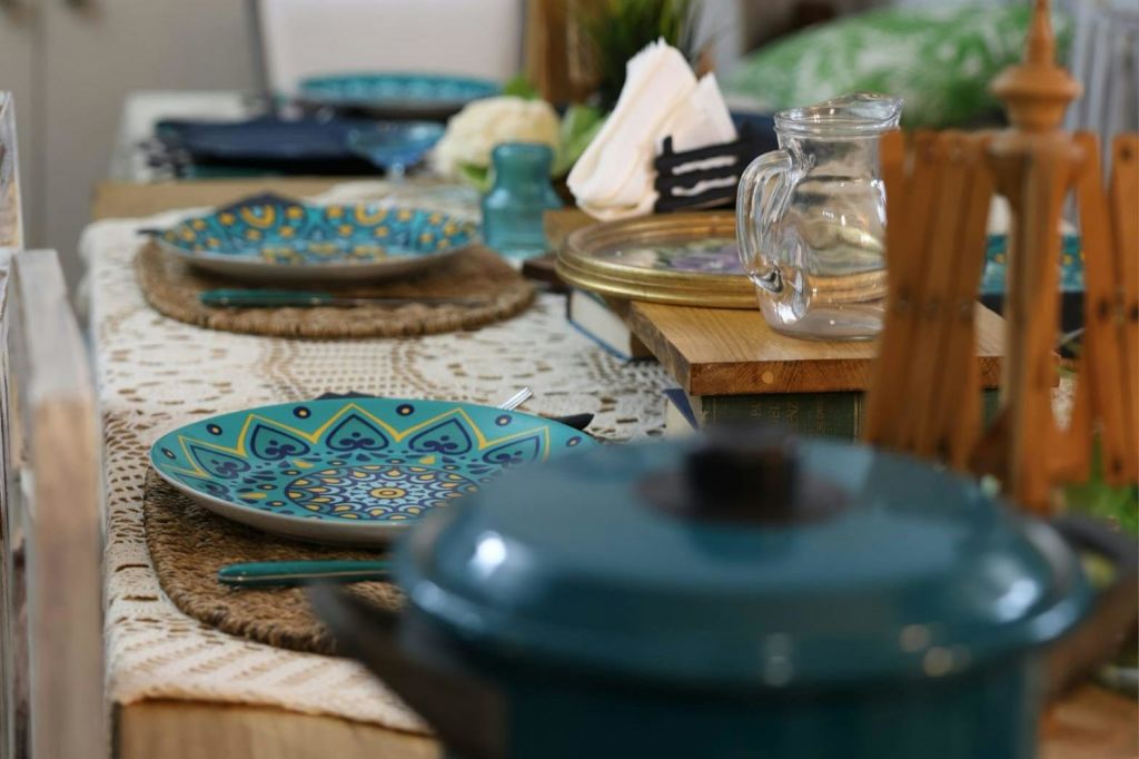 다채로운 접시, 유리 투수, 접힌 냅킨, 전경에 파란색 냄비 뚜껑이 있는 테이블 세트.