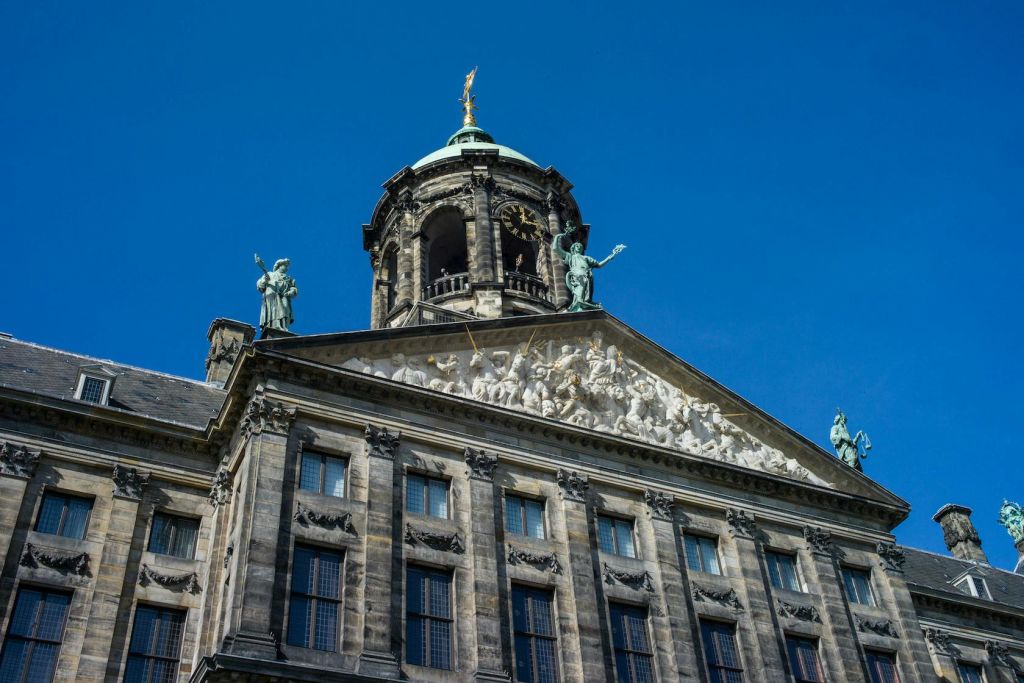 맑고 푸른 하늘을 배경으로 시계탑과 돔이 있는 동상과 부조 조각이 있는 화려한 건물 외관.