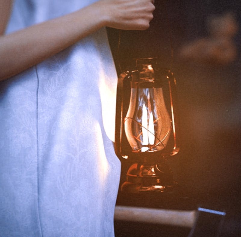 밝은 파란색 드레스를 입은 사람이 희미한 조명 속에서 빛나는 등불을 들고 있습니다.