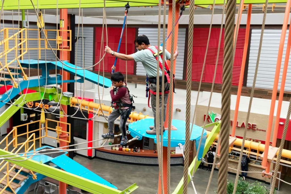 안전 하네스를 착용하고 다채로운 실내 로프 코스를 항해하는 어린이와 성인.