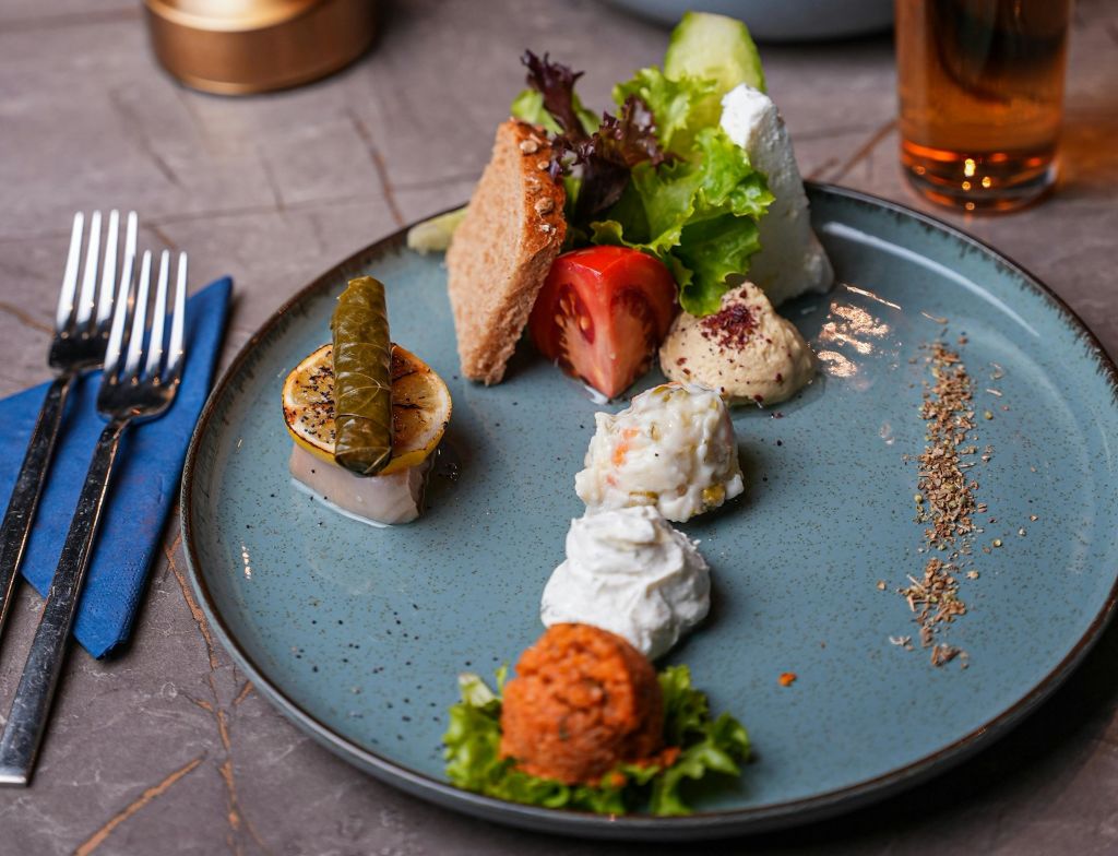 도금된 애피타이저에는 돌마, 후무스, 자트지키, 샐러드, 빵, 파란색 접시에 토마토 슬라이스 등 다양한 작은 서빙이 있습니다.