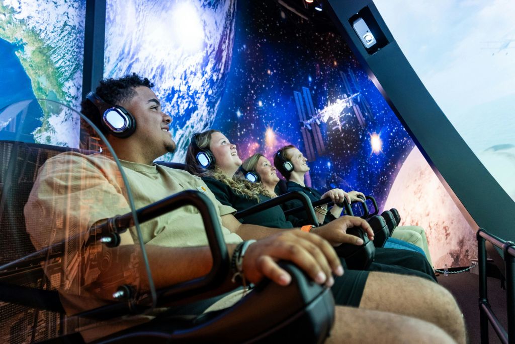 네 명의 사람이 헤드폰을 끼고 의자에 앉아 우주에서 지구를 바라보고 있습니다.
