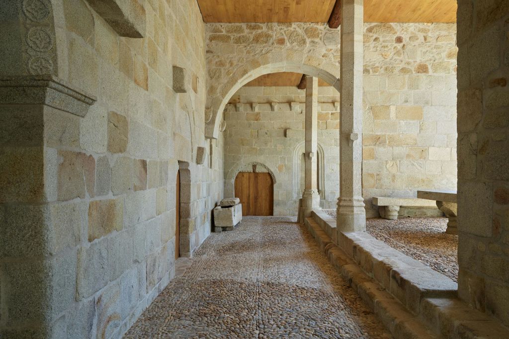 아치형 출입구와 기둥, 나무 문이 있는 석조 복도. 바닥은 자갈로 만들어져 있습니다.