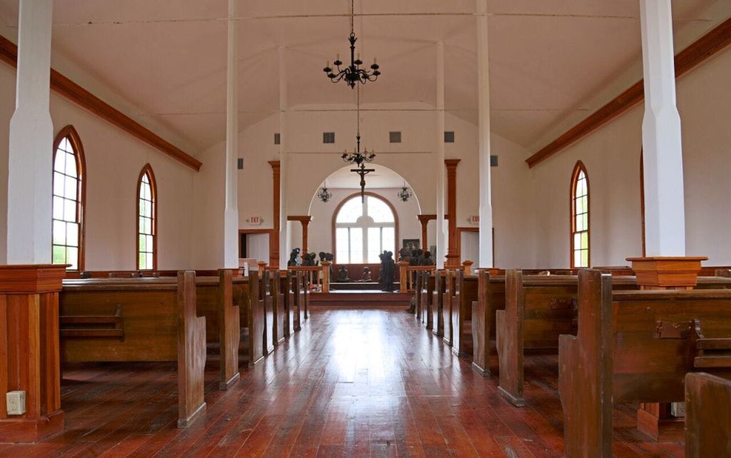 정면에 목조 페우, 샹들리에, 아치형 창문, 높이 솟은 제단이 있는 교회 내부.