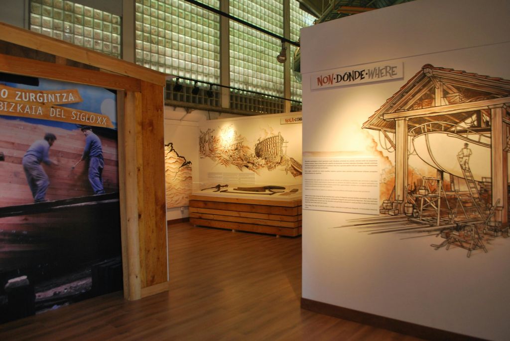 일러스트레이션, 텍스트 패널, 건축 모델이 있는 박물관 전시실. 표지판에는 나무 악센트가 있는 "NON-DONDE-WHERE" 라고 쓰여 있습니다.