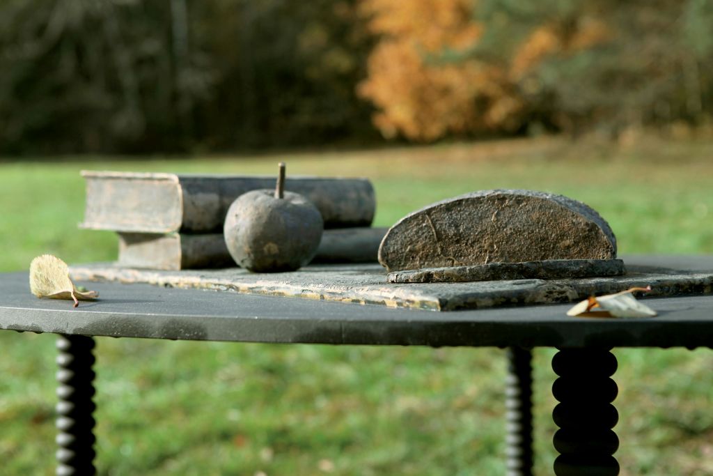 나무와 잔디가 있는 가을을 배경으로 오래된 책, 둥근 돌, 부서진 연마석이 놓인 야외 테이블.