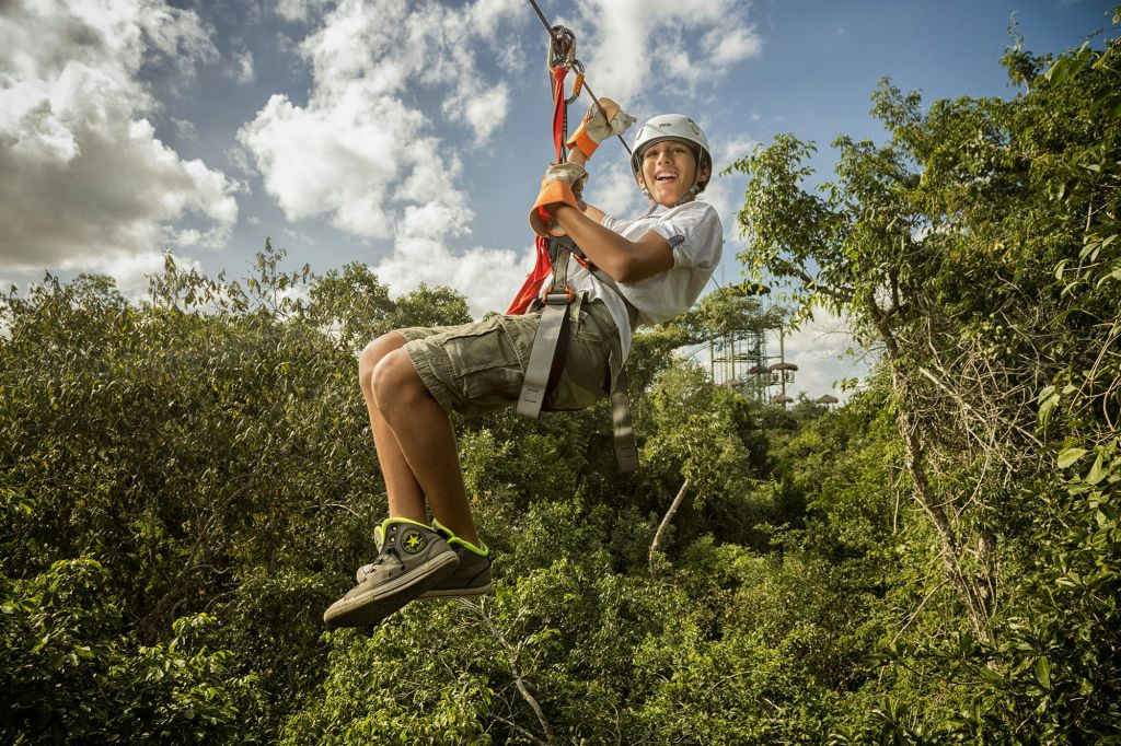 헬멧과 하네스를 착용한 사람이 숲을 가로질러 플랫폼을 배경으로 집업을 하고 있습니다.