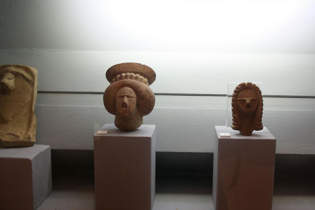 박물관 환경에서 집중 조명 아래에 머리 장식이 있는 작은 돌 조각이 받침대에 전시되어 있습니다.