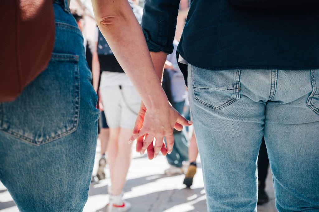 두 사람이 손을 잡고 군중 속을 걷고 있습니다. 둘 다 청바지를 입고 허리 아래로 보입니다.